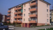4-story apartment building with orange and beige exterior, balconies on each unit, and a parking area in front