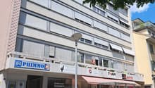 concrete and glass building, multiple windows, sign reads Phimmo, awnings, store front, lamp post, scooters, trash cans, bicycles