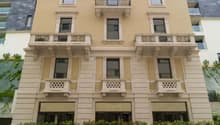 3 story building with beige paint, black iron balconies, window grills, greenery at the bottom