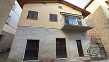 2 story house, stone facade, raised ground floor, balcony, two large wooden doors, stone steps