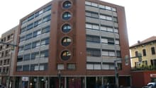Multi-story brick building with large windows, circular window patterns, and ground-level retail spaces