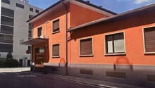 2-story orange building with large windows, located on a street with other buildings in the background