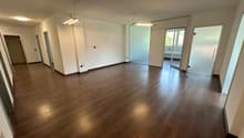 Empty room with wooden floors, white walls, and glass doors leading to another room.