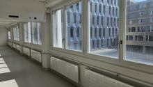 Empty office room with large windows, radiators, grey flooring