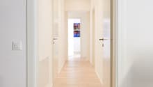 Empty corridor with hardwood floor, white walls, recessed ceiling lighting.