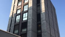 High-rise building, grey stone walls, multiple windows, ground floor with garage entrances