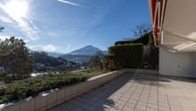 Outdoor terrace with tiled flooring, surrounded by greenery and a view of the mountains.