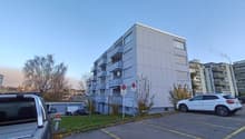 large building with many balconies, white walls, multiple floors, and parking lot in front