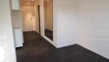 Empty room with white walls and gray flooring, a large mirror is mounted on the wall.
