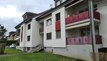Multi-story apartment building with white exterior walls, red and yellow accents, and balconies with red railings.