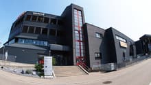 Three-story office building, black exterior, red accents, large windows, stairs leading to entrance, plants and rocks outside.