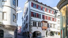 Three story commercial building, red shutters, central arched entrance, shops on the ground floor