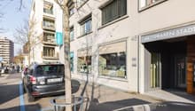 Two-story residential building, modern design, shops on the ground floor, balcony on the upper floor, white facade, parking space