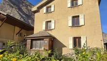 two-story stone house, white shutters, large flower beds with yellow flowers, stunning mountain views
