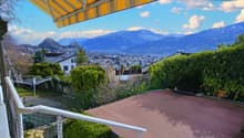 outdoor terrace with awning, railing, wooden floor, bushes, net, cityscape view, mountains in the distance