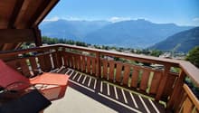 wooden balcony with lounge chair, wooden railing, panoramic mountain view, grassy slope below