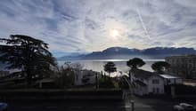 Wide view of a road, lake, mountains, white houses, road, trees, sky with clouds