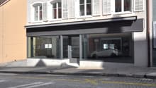 Storefront with glass windows, white shutters, black awning, white car visible inside