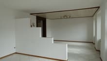 Empty room with white walls, white tiled floor, wooden trim, and a ceiling with lights.