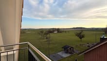 balcony with railing, green field, distant house, small shed, clear sky, metal railing