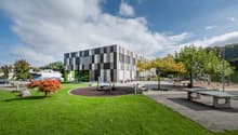 Modern architectural building with checkered facade, located outdoors, surrounded by a lawn, playground, and trees.