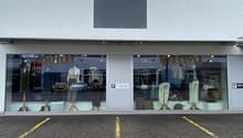 Storefront with glass windows and parking area in front, mannequins and displayed clothes inside