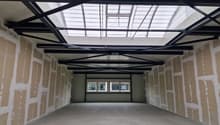 Empty room with concrete floor, unfinished walls, metal roof structure, and windows