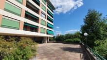 Large building with multiple floors, brick facade, multiple balconies, parking area, green awnings