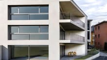 3-story modern apartment building with large windows, balconies, and a small outdoor seating area on the ground floor