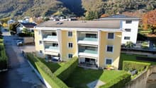 3-story apartment building, yellow exterior, multiple balconies, green hedges, solar panels on the roof, mountain view