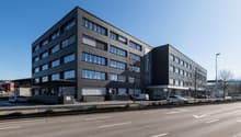 modern office building with multiple windows, concrete facade, ground floor entrance, parking area