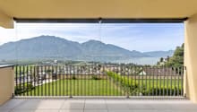 large glass walls, metal railing, tiled floor, distant view of city, mountains and lake