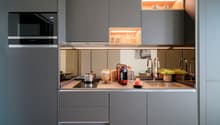 Modern kitchen with gray cabinets, wooden countertop, built-in Siemens microwave oven, various kitchen appliances and utensils, open shelving with decorative items