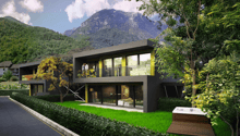 Modern two-story house with large windows, black exterior, surrounded by lush greenery and mountains in the background. The house has a balcony or terrace overlooking the scenic landscape.