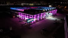 Large commercial building with colorful LED lighting on the exterior, parking lot in the foreground, and a sign for 'Arbor Park' visible.