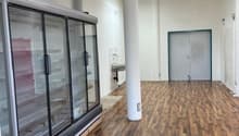 Large open space with hardwood floors, glass display refrigerators, and a door leading to another room.