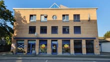 3 story building, blue trim, round windows, commercial windows, 3 entrances, barrel outside, plants