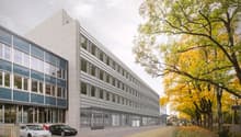 Office building with 3 floors, glass windows, Tesla branding, paved road, trees, and parked cars