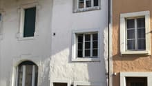 A white building with a brown door, two brown windows, and a brick wall