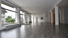 Large open space, hardwood floors, large windows, bench, and industrial-style interior design.
