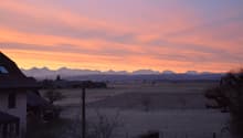 a two story house with an orange sky in the background and mountains on the horizon