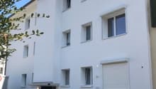 Multi-story building, white exterior, multiple windows, entrance with canopy, some items stored outside