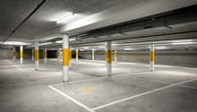 Concrete floor, yellow and white columns, designated parking spaces, disabled parking symbol, white lines marking parking spots, fluorescent lighting.