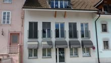 white building, brown roof, multiple windows, balconies, awnings, entrance door