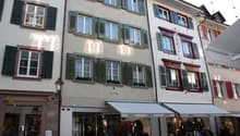 3 story building, white walls, green shutters, red trim, multiple windows, shops on the ground floor