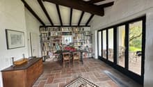 Dining room with wooden table, chairs, bookshelves, brick floor, sliding glass doors, picture frame, flowers, rug, wooden cabinet, outdoor seating