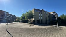 apartment building, large paved square, several trees, street lights, sunny day