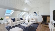 Spacious living room with vaulted ceiling, skylights, white sofa and armchair, coffee table, area rug, and a fireplace