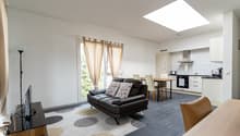 dark leather sofa, round coffee table, large rug, large white windows, white kitchen with kitchen island and breakfast table