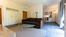 modern living area with a couch, glass coffee table, rug, modern kitchen with dining table, and microwave